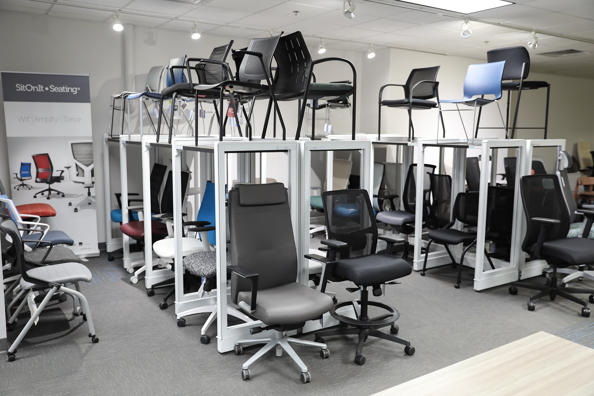 Office seating display inside the Holland, MI showroom, showing a variety of chairs arranged on white platforms.