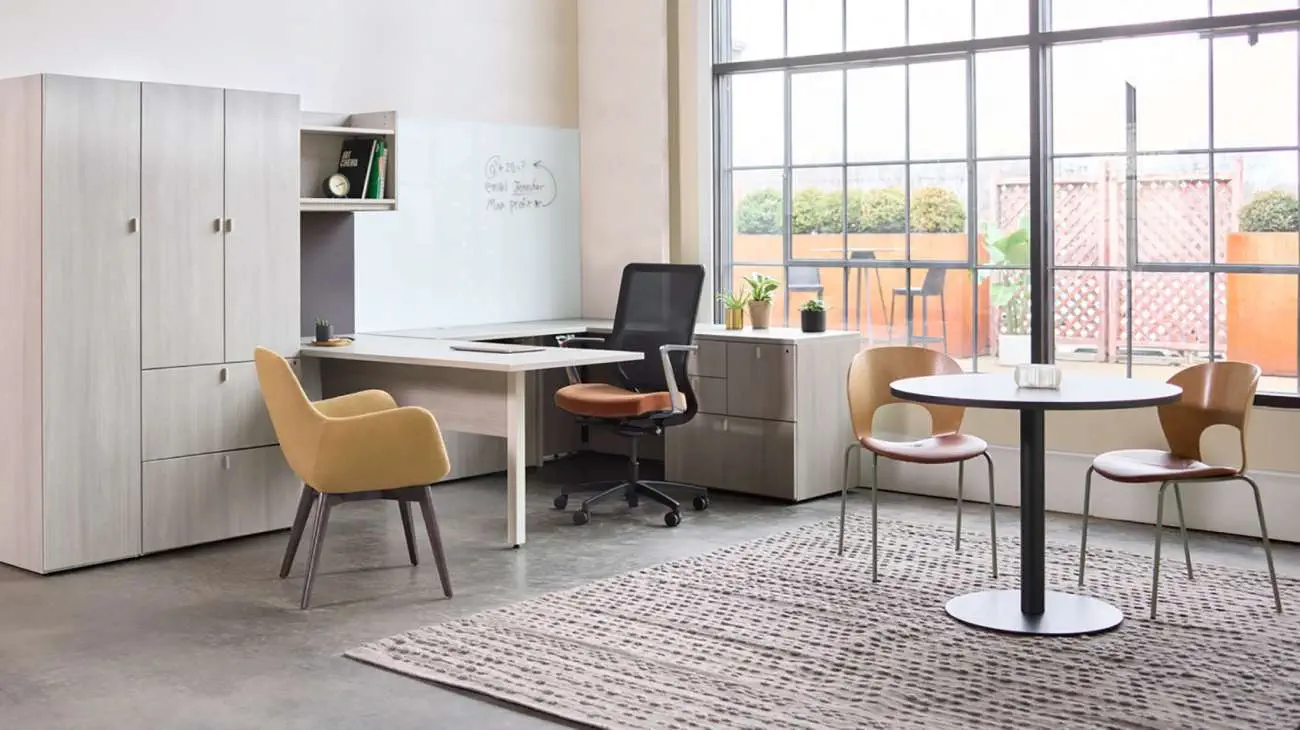 OFS Pulse desk in light wood finish with integrated storage cabinets and overhead shelving, styled in a modern office with guest seating and large industrial-style windows.